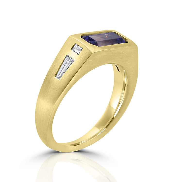 andmade yellow gold ring featuring a vibrant emerald-cut tanzanite gem with baguette diamonds on the sides and a matte satin finish