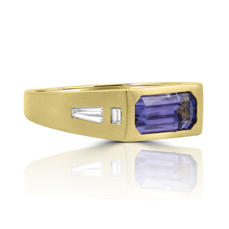 andmade yellow gold ring featuring a vibrant emerald-cut tanzanite gem with baguette diamonds on the sides and a matte satin finish