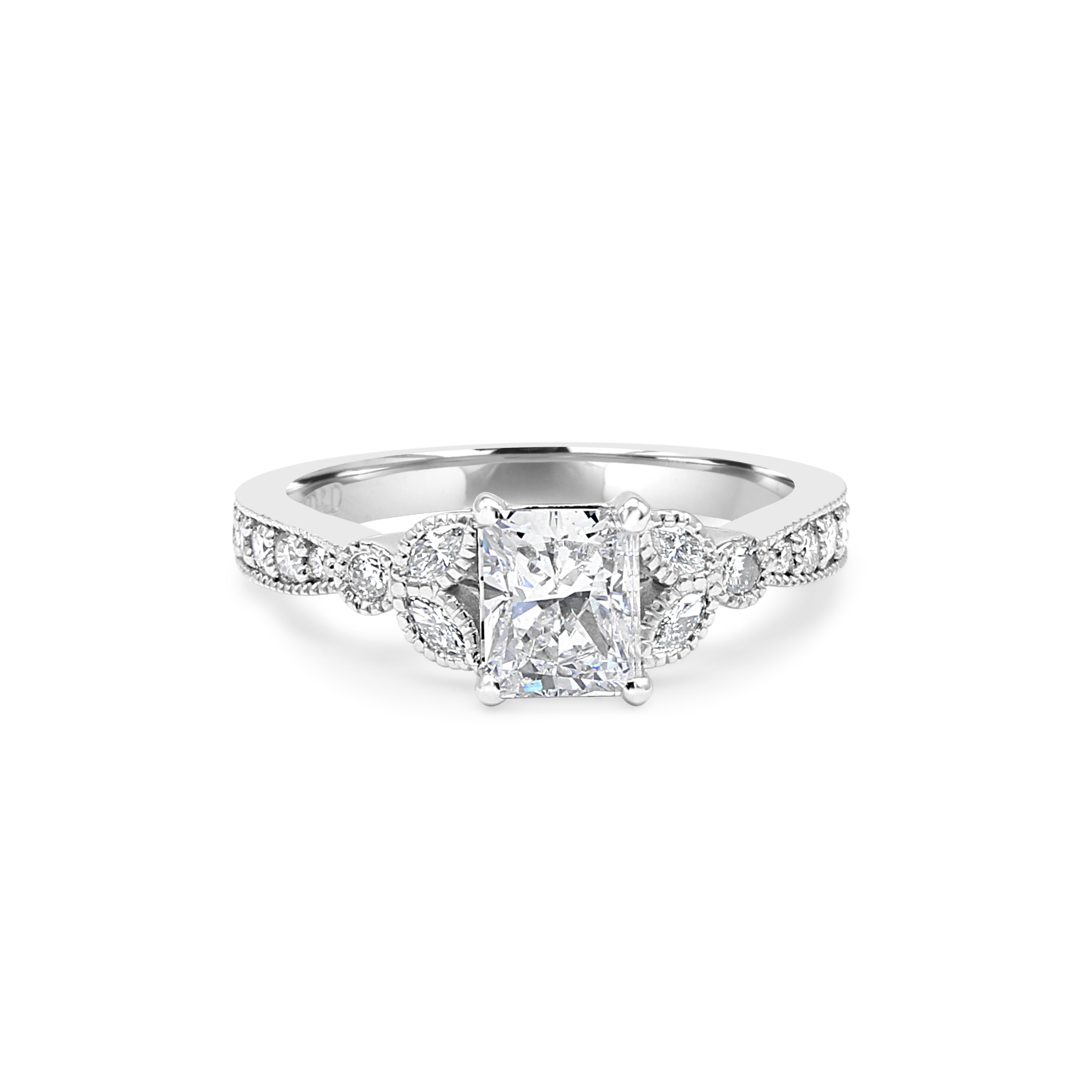 Radiant-cut center diamond surrounded by accent diamonds, featuring a millgrain detail on the shank.