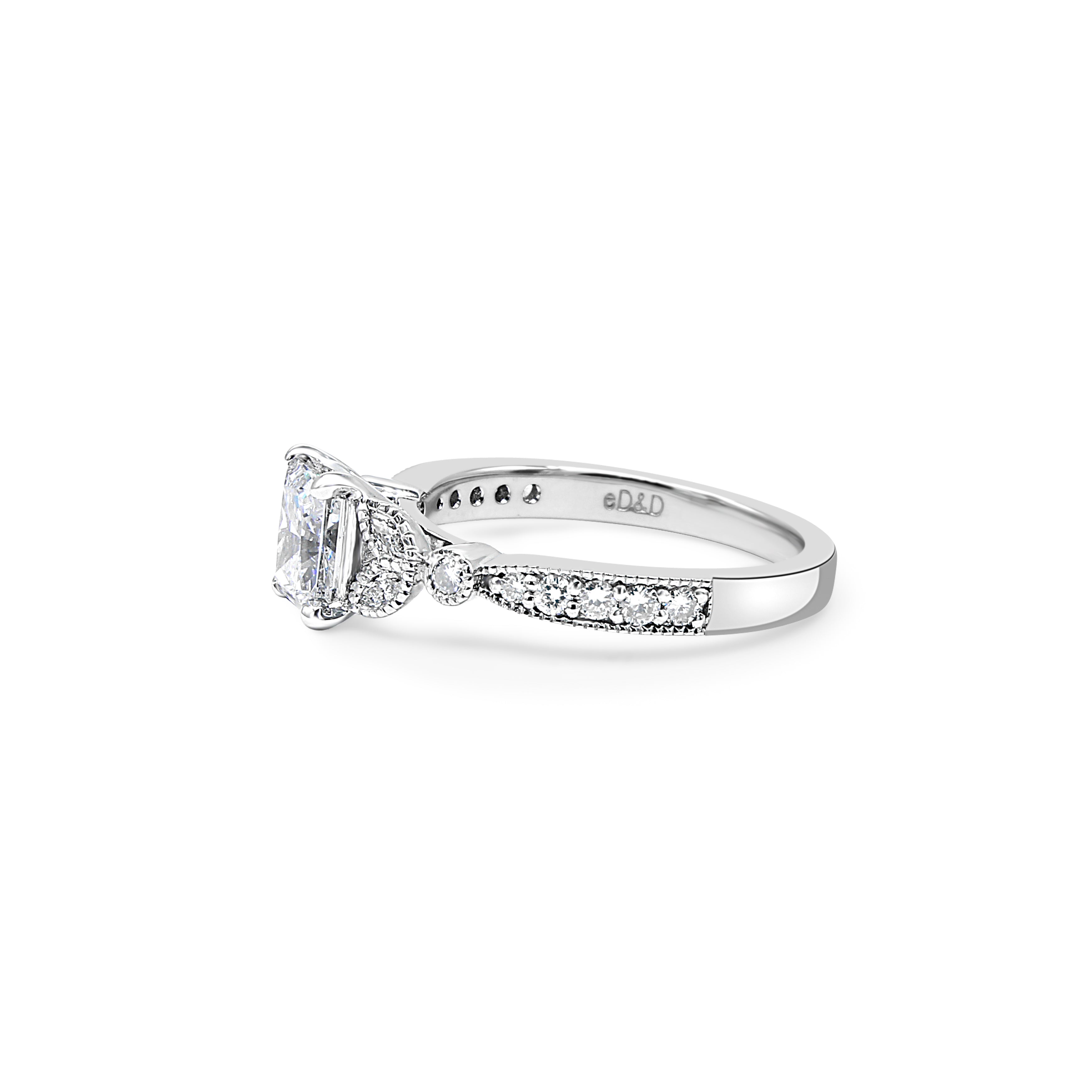 Radiant-cut center diamond surrounded by accent diamonds, featuring a millgrain detail on the shank.